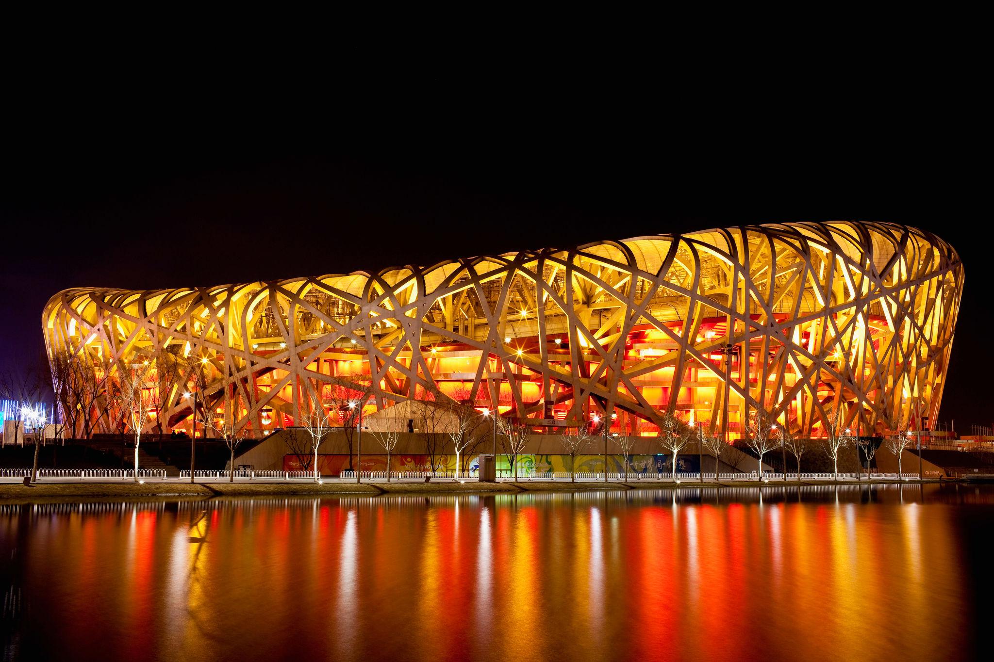 Modern stadium with a unique architectural design illuminated at night, reflected in water.